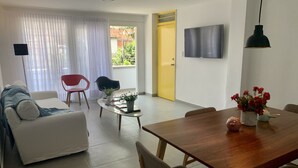 Una sala de estar moderna con un sofá, una mesa de comedor y un televisor montado en la pared.