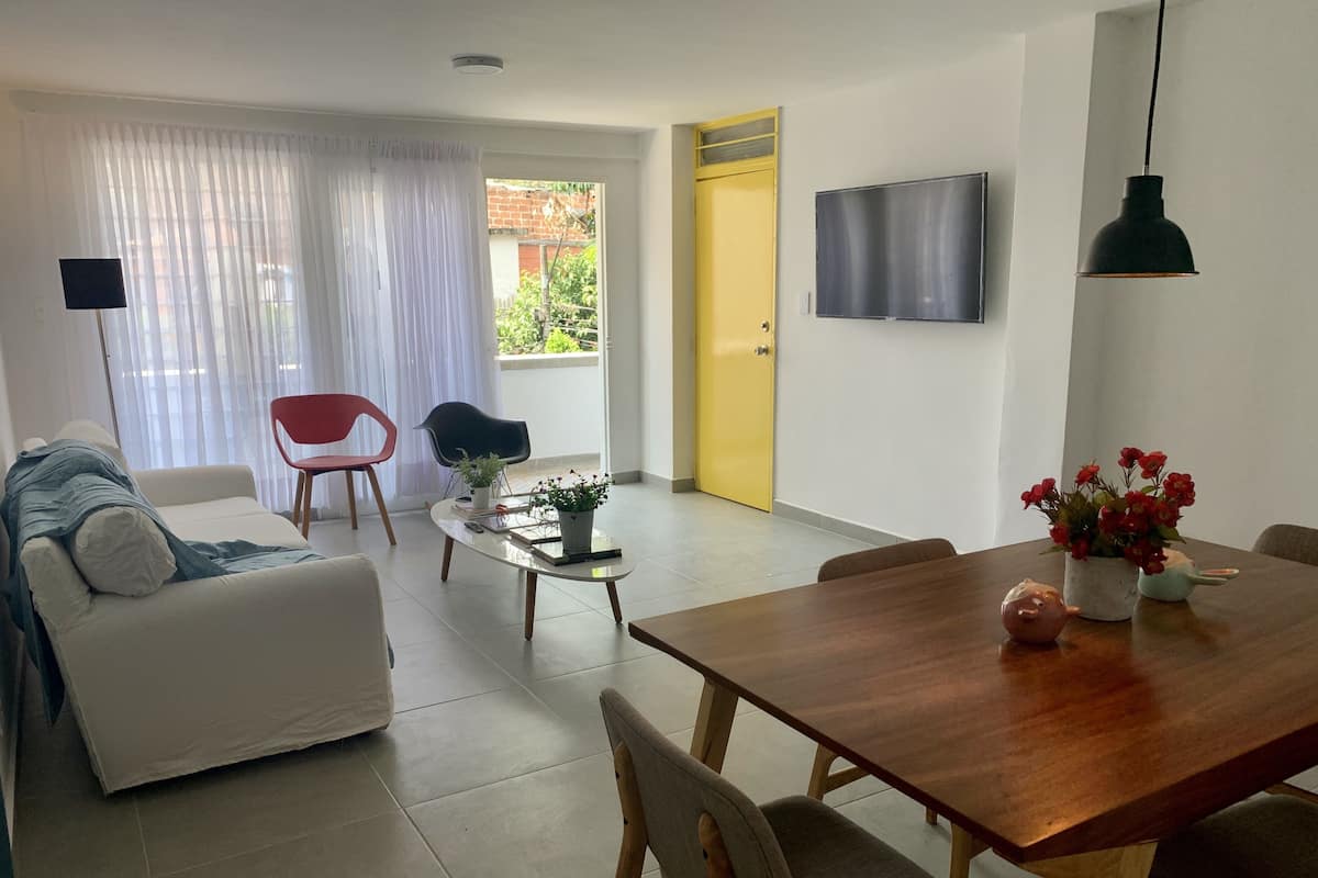 Una sala de estar moderna con un sofá, una mesa de comedor y un televisor montado en la pared.