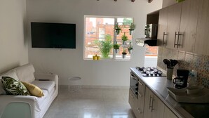 Una cocina moderna con un televisor de pantalla plana, una zona de comedor con un sofá blanco y una ventana con plantas en macetas.