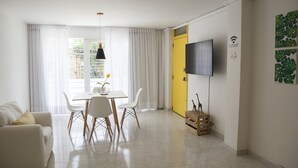 Un salón moderno con comedor, una puerta amarilla, un televisor de pantalla plana y una planta en la pared.