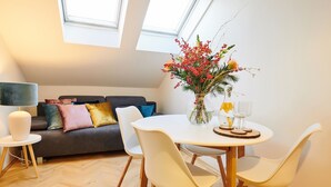 Un salon moderne avec un canapé gris, des coussins colorés, une table à manger blanche avec des chaises, un vase rempli de fleurs et une lampe.