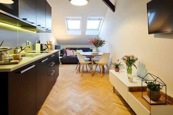 A modern kitchen with a herringbone floor, a dining area with a round table and chairs, and a TV mounted on the wall.