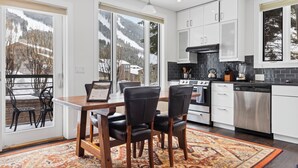 A modern kitchen with white cabinets, a stainless steel oven, and a dishwasher. There is a dining area with a wooden table and black chairs. - Outpost: King Ridge 4 - AC & Hot Tub! (Jackson)