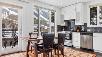 A modern kitchen with white cabinets, a stainless steel oven, and a dishwasher. There is a dining area with a wooden table and black chairs.
