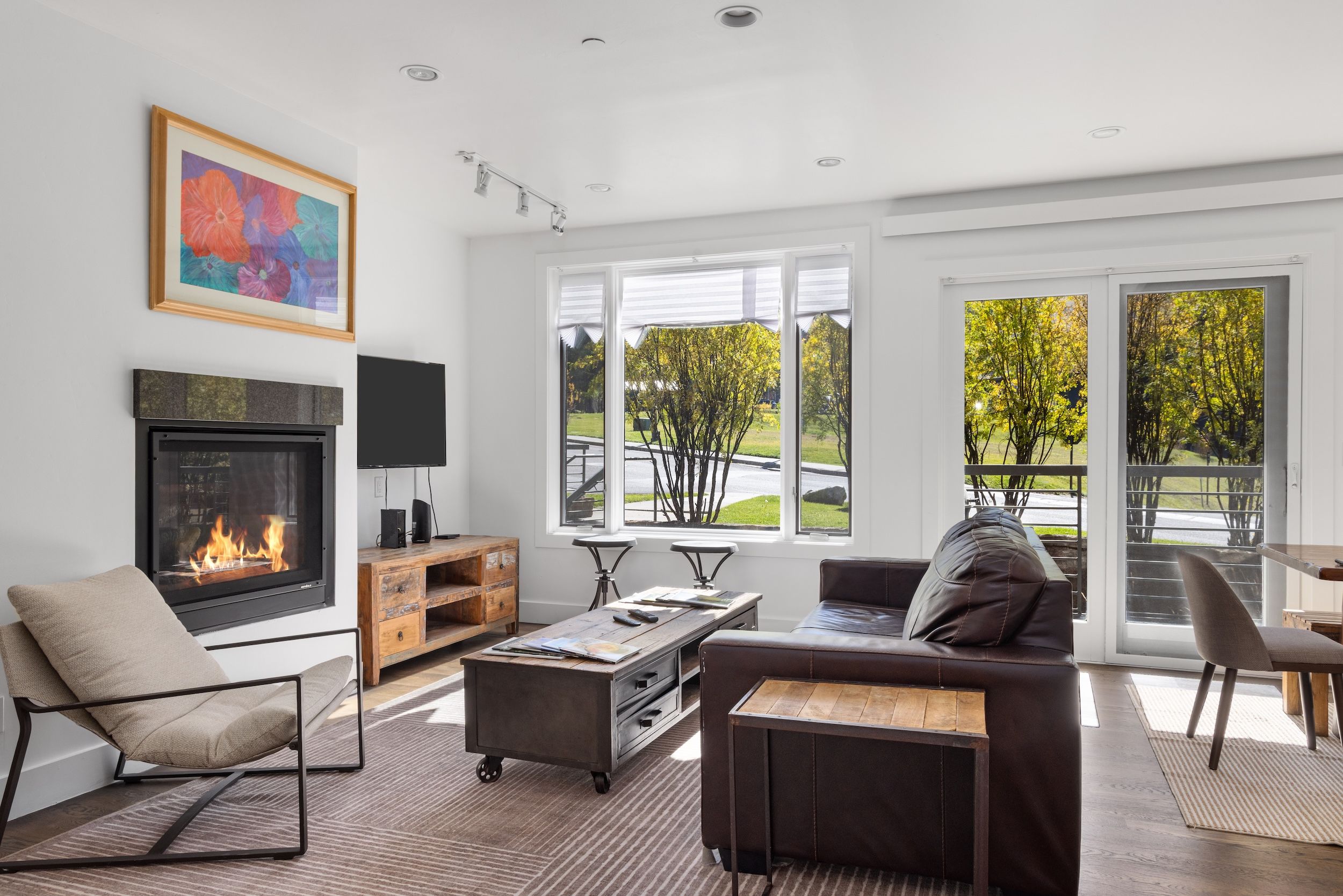 Una sala de estar moderna con chimenea, televisor y un gran ventanal con vistas a un jardín.
