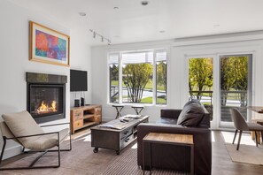 Una sala de estar moderna con chimenea, televisor y un gran ventanal con vistas a un jardín.