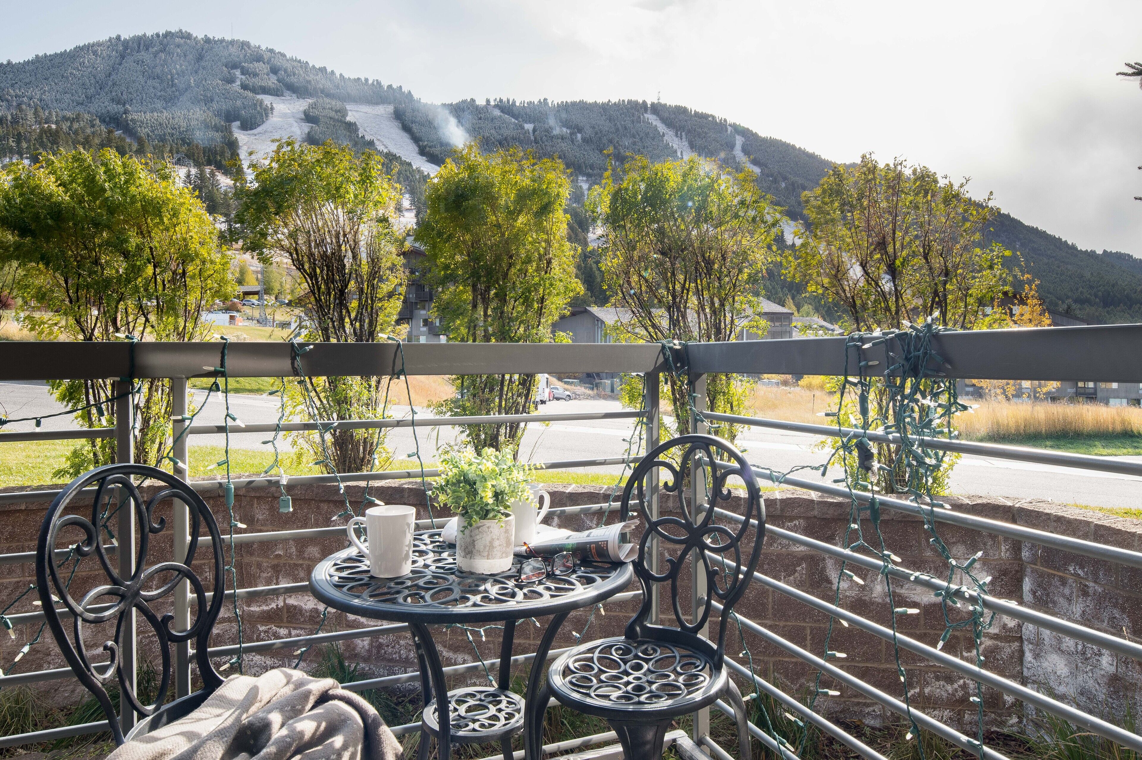 A balcony with a table and chairs, overlooking a mountainous landscape with trees and a road.
