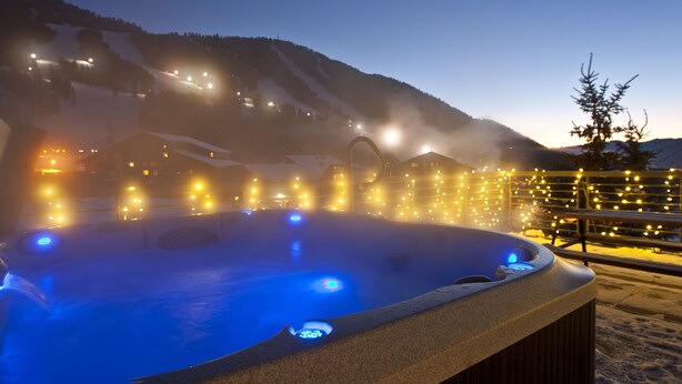 A hot tub with blue lights, surrounded by snow-covered mountains and a wooden fence with string lights. - Outpost: King Ridge 4 - AC & Hot Tub! (Jackson)