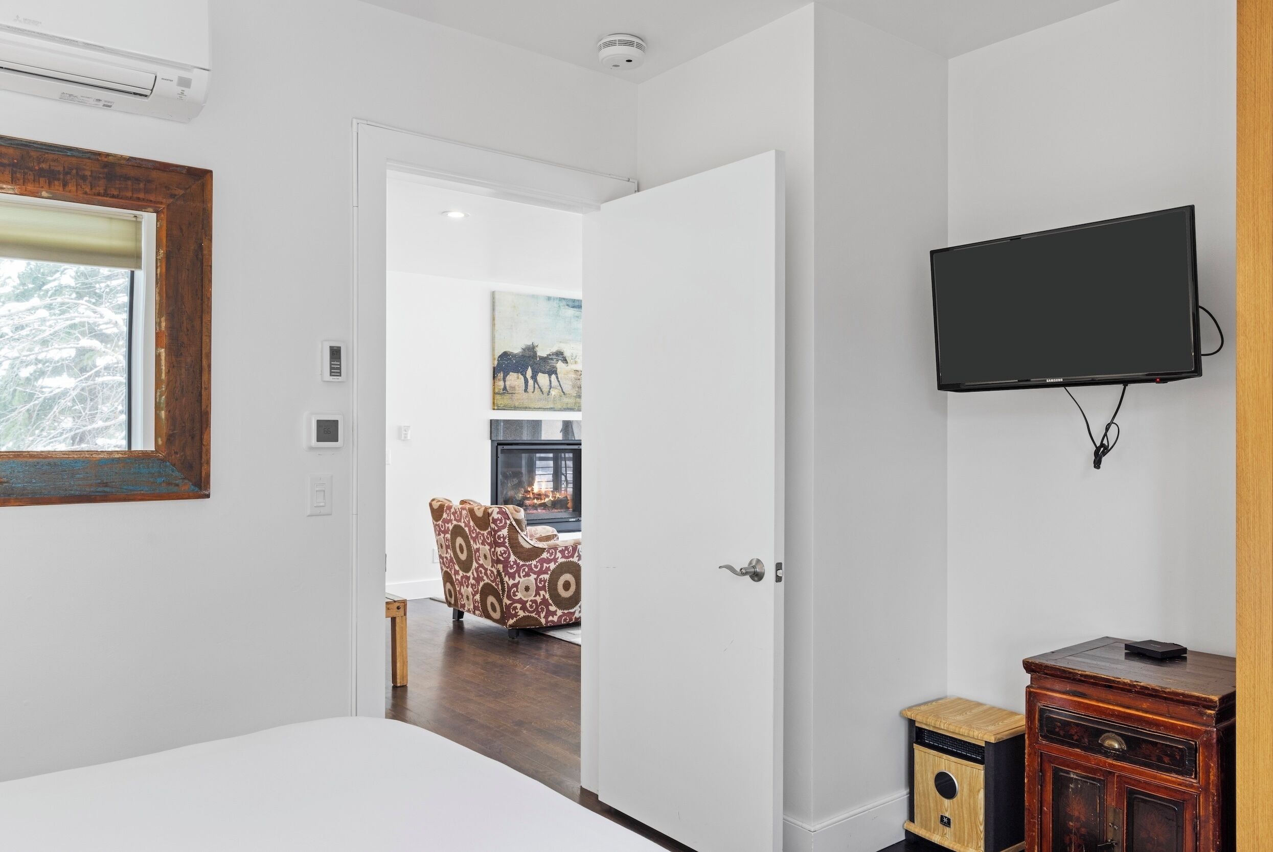 A modern hotel room with a bed, a TV mounted on the wall, a wooden cabinet, and a door leading to another room.