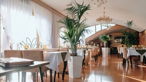 A spacious dining area with multiple tables and chairs, large potted plants, and elegant chandeliers. - Bayil Breeze Hotel (Baku)