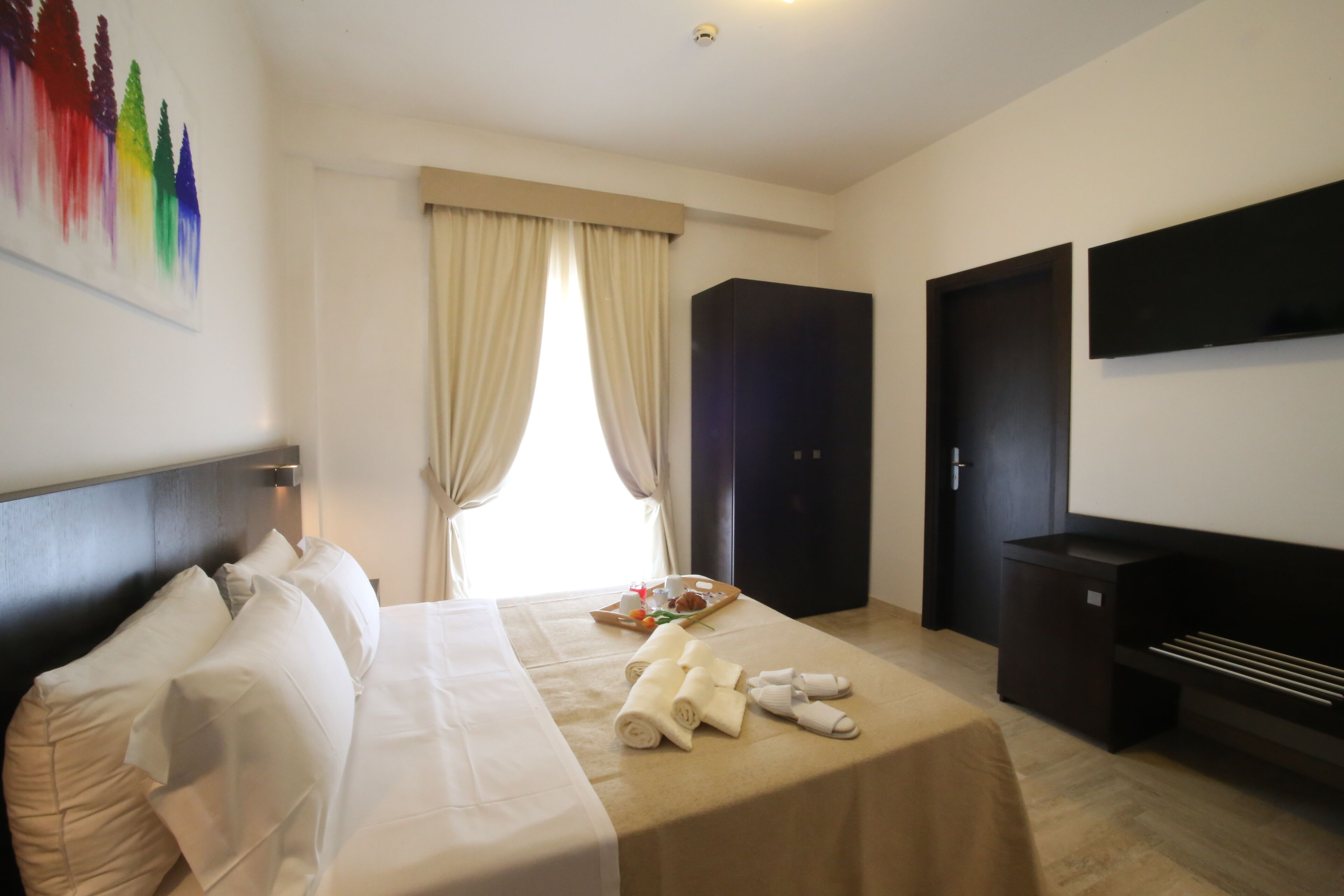 Una habitación de hotel con cama, televisor, armario y ventana con cortinas.