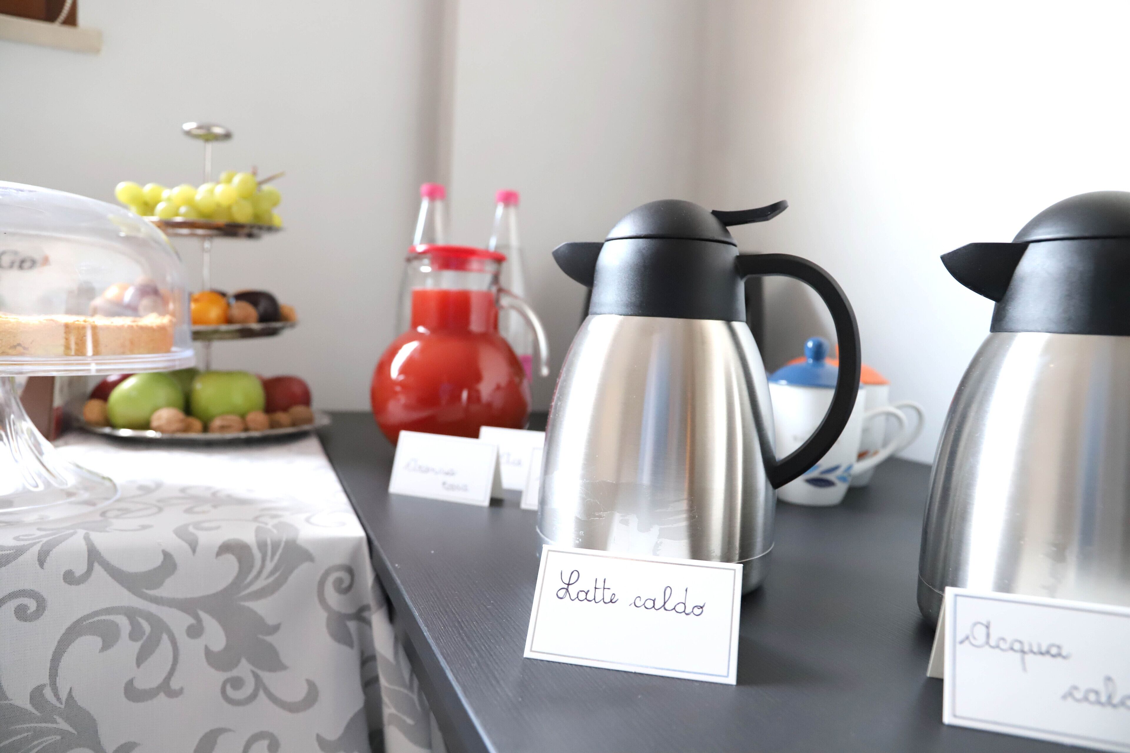 A buffet table with labeled coffee and water dispensers, a fruit display, and a covered dessert dish.