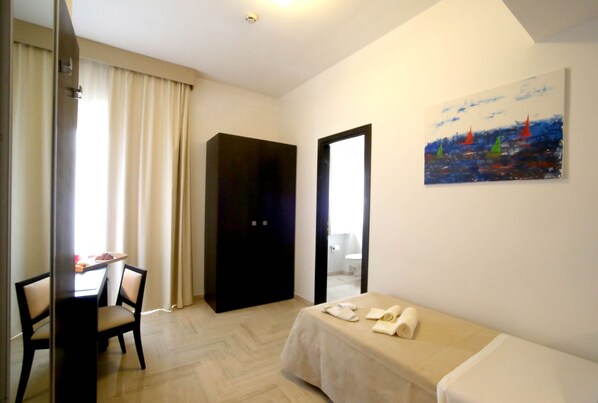 A hotel room with a bed, a dining table with chairs, a painting on the wall, and a door leading to a bathroom. - Albergo Cantiani (Ancona)