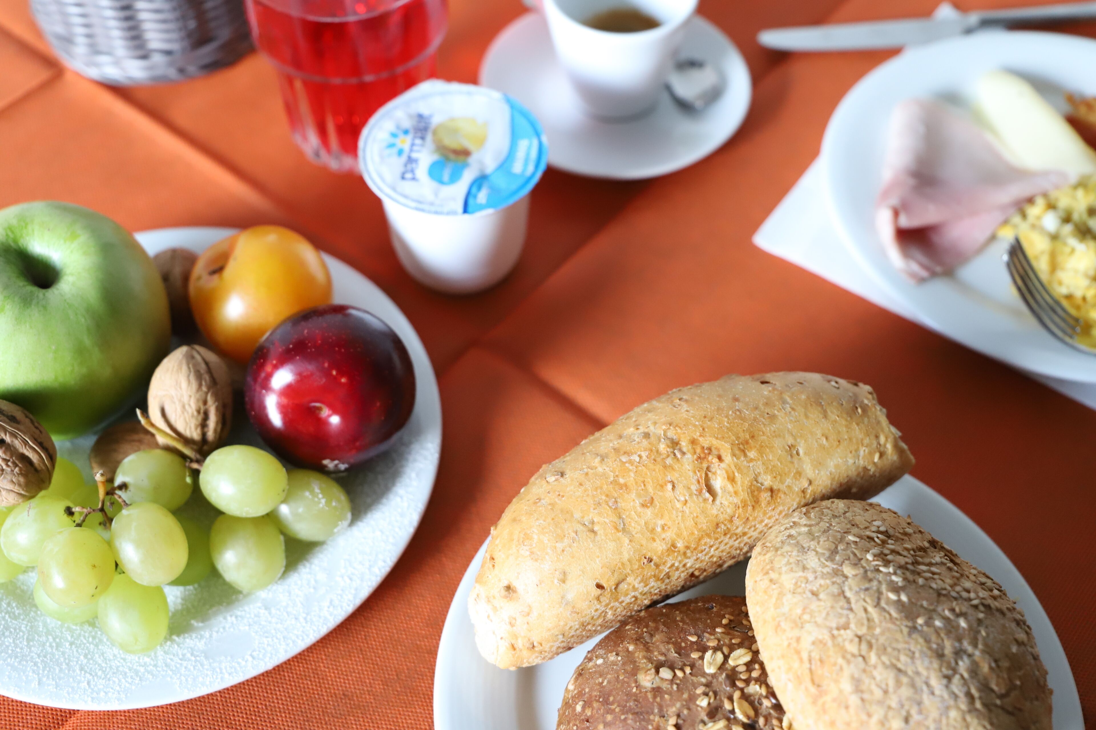 Une table mise pour le petit-déjeuner avec une assiette de fruits, un verre d’une boisson rouge, une tasse de café et deux sortes de pain.