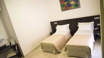 Una habitación de hotel con dos camas individuales, un escritorio con silla y una mesita de noche con lámpara.