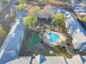 Vista aérea de una zona residencial con piscina, un pabellón y un pequeño parque con bancos.