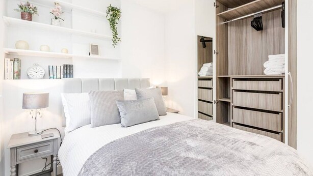 A modern bedroom with a bed, bedside tables, a wardrobe, and shelves with decorative items. - Flat 5 · Stunning 2-Bed Notting Hill Portobello Apartment (London)