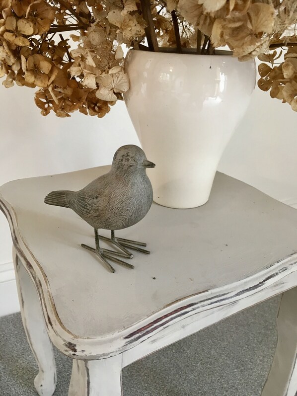 A bird figurine on a white table with a vase of dried flowers in the background. - Self Contained stay, close to town & country, ample parking, beautiful grounds. (Horsham)