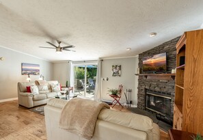 A living room with a fireplace, a ceiling fan, and a view through a glass door to an outdoor area. - East Asheville - Views - Fire Pit - Parkway - Hiking - Pets - Wi-Fi - Large Home (Asheville)