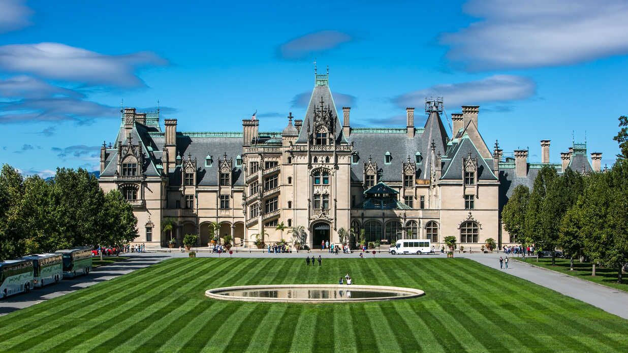 A large, historic building with a central courtyard, surrounded by well-manicured lawns and a reflective water feature.