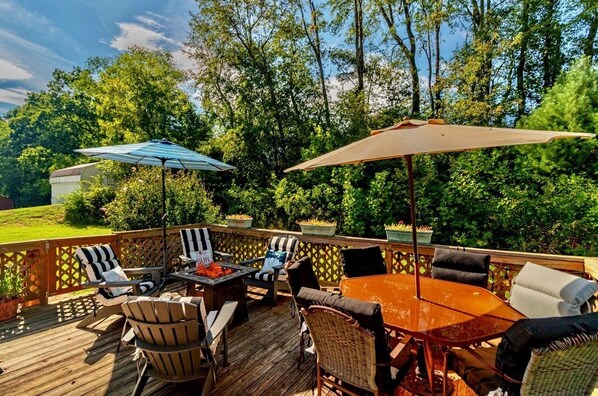Une terrasse extérieure avec une table et des chaises en bois, entourée d’une végétation luxuriante et d’arbres.