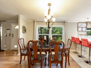 A dining area with a wooden table and chairs, a chandelier, and a window with a view of greenery. - East Asheville - Views - Fire Pit - Parkway - Hiking - Pets - Wi-Fi - Large Home (Asheville)