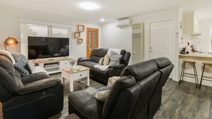 Un salon moderne avec un canapé, une table basse et un téléviseur. Il y a également un coin cuisine avec un comptoir et des tabourets.