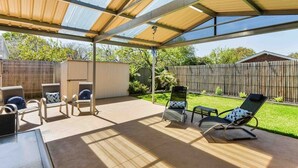 Un patio couvert aménagé avec du mobilier d’extérieur, notamment des chaises et une table, et offrant une vue sur le jardin arrière.