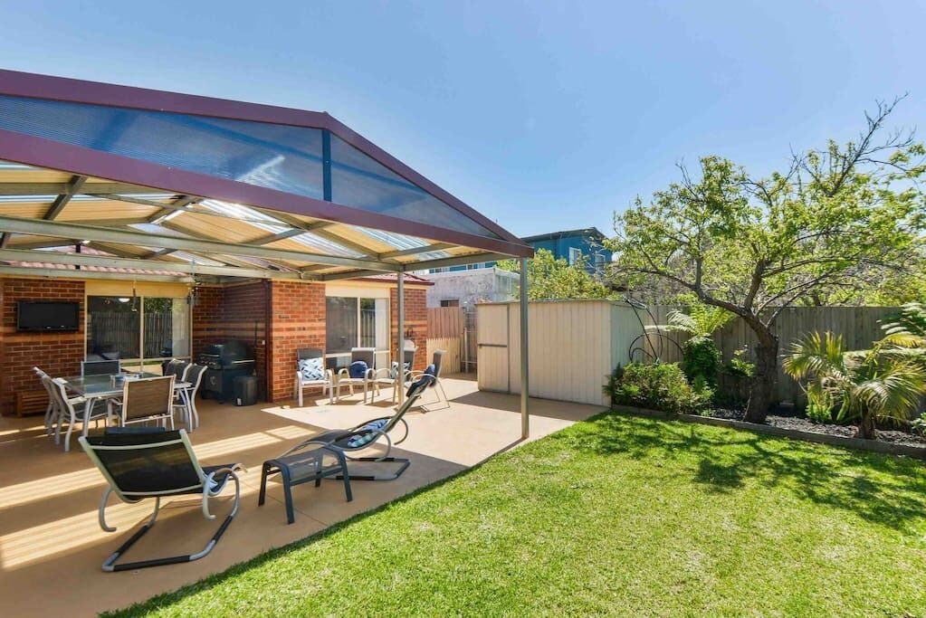 A covered patio with outdoor furniture, a barbecue grill, and a well-maintained lawn.