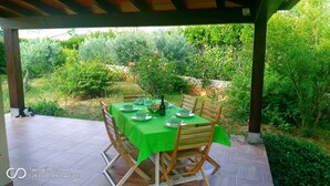 An outdoor dining area with a table set for four, surrounded by lush greenery and a stone wall. - Viviholidays your holiday villa (Castellammare del Golfo)