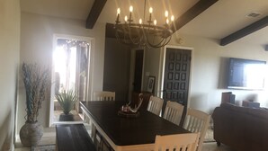 A dining area with a dark wooden table, white chairs, a chandelier, and a large window with curtains.
