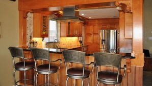 A kitchen with wooden cabinets, a stainless steel refrigerator, and four bar stools.
