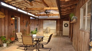 A wooden patio with a table and chairs, a ceiling fan, and a door with a wreath.