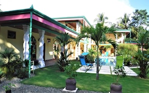 Un hotel con piscina, mobiliario exterior y abundante vegetación.