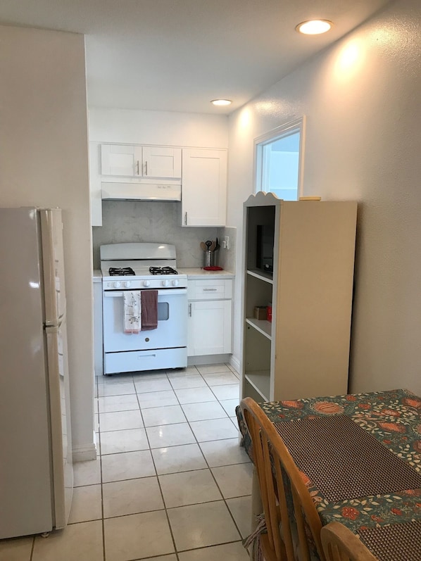 A compact kitchen with white cabinets, a stove, and a refrigerator.