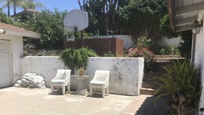 A concrete patio with two white lounge chairs and a small round table, surrounded by potted plants and a basketball hoop. - Entire 3 bedrooms guest property, near Pacific Beach, Downtown，Seaworld，LaJolla (San Diego)