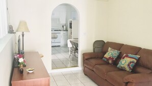 A living room with a brown sofa, a wooden coffee table, and a lamp. There is a doorway leading to a kitchen area. - Entire 3 bedrooms guest property, near Pacific Beach, Downtown，Seaworld，LaJolla (San Diego)
