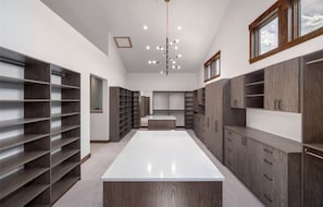 A spacious walk-in closet with multiple shelves and cabinets, a central white platform, and a ceiling light fixture.