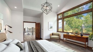 Une chambre à coucher moderne, avec un lit, une chaise, une commode en bois et une grande fenêtre donnant sur des arbres.