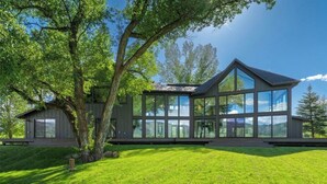 Une maison moderne dotée d’une grande façade vitrée, d’un toit en pente et d’une pelouse bien entretenue.