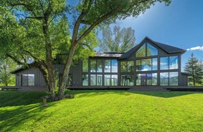 Een modern huis met een grote glazen pui, een schuin dak en een verzorgd gazon.