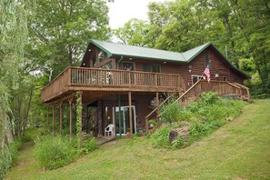 A log cabin with a wooden deck and a staircase leading to a porch. - Riverside Chalet, LLC (Muscoda)