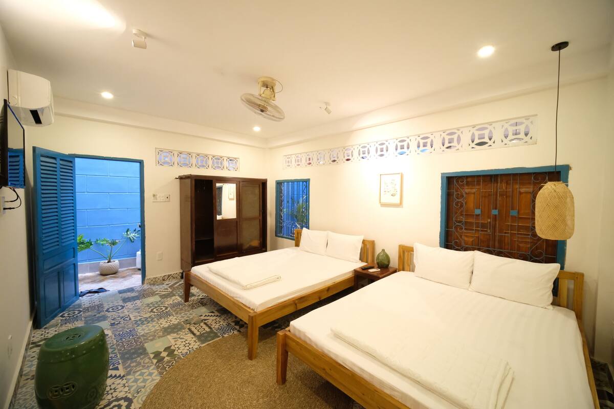 A hotel room with two beds, a small table, a wall-mounted fan, and a potted plant.