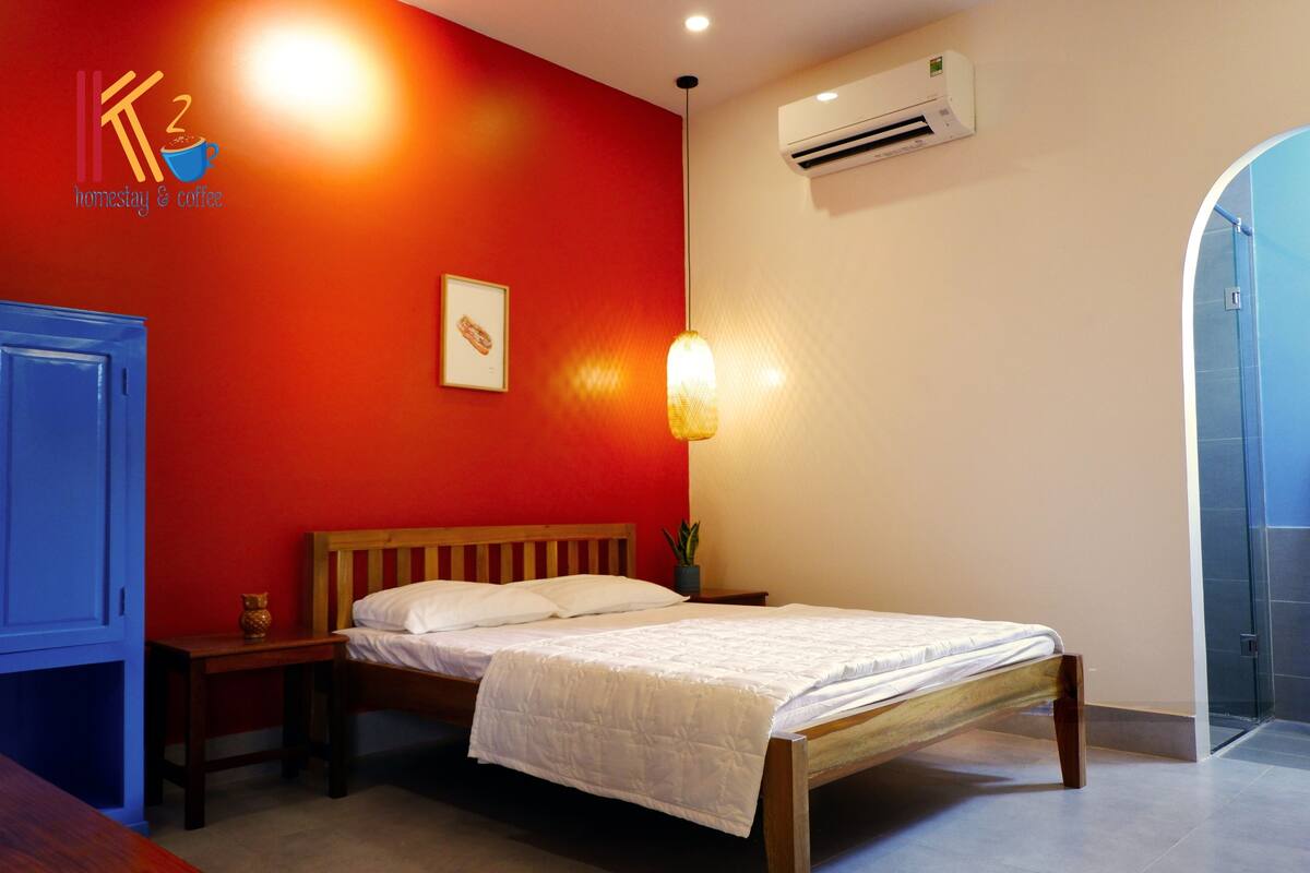 A bedroom with a wooden bed, a nightstand, a wall-mounted air conditioner, and a door to a bathroom.