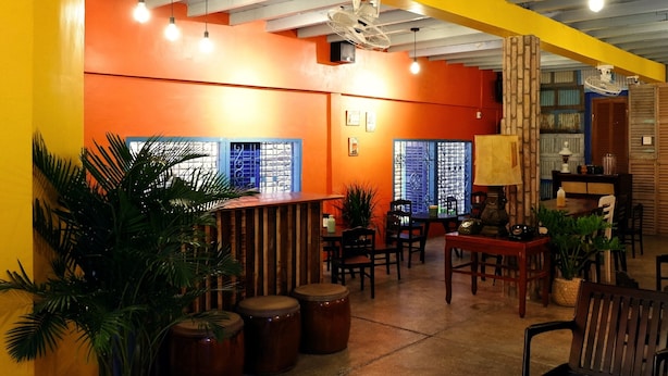 A brightly lit interior with orange walls, wooden furniture, and potted plants. - K2 Homestay & Coffee - Hostel (Can Tho)