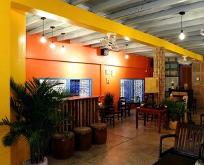 A brightly lit interior with orange walls, wooden furniture, and potted plants. - K2 Homestay & Coffee - Hostel (Can Tho)