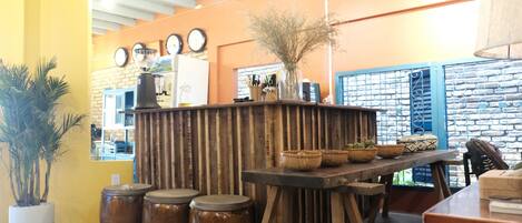 A rustic interior with a wooden counter, stools, and a potted plant.