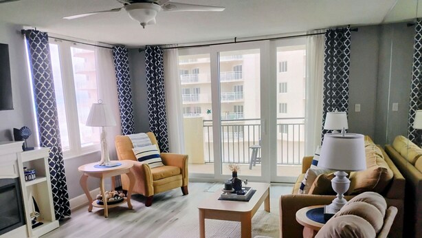 Un salon moderne avec un canapé, un fauteuil et une table basse. Il y a un balcon qui offre une vue sur l’immeuble.