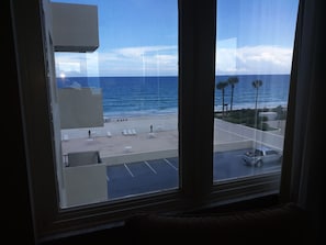 A view from a window overlooking a beach with lounge chairs and a parking area.