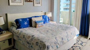 Une chambre à coucher avec un lit, des tables de chevet, une lampe, une fenêtre avec des rideaux et des tableaux encadrés accrochés au mur.